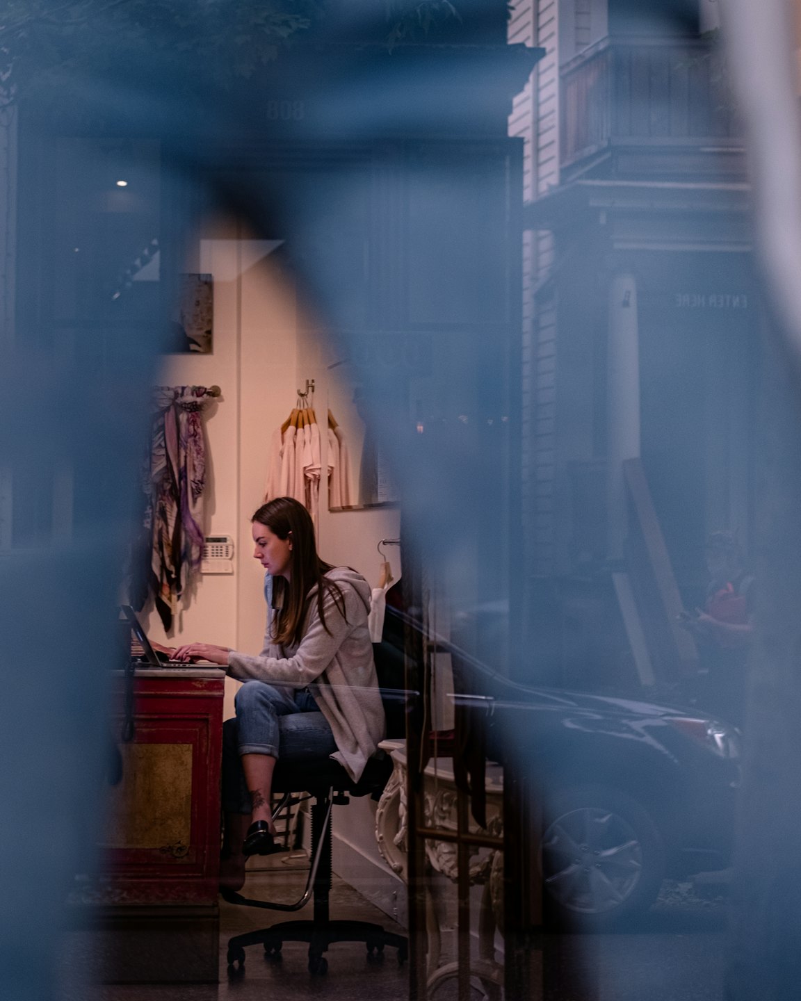 Woman works on laptop at red desk in shop.