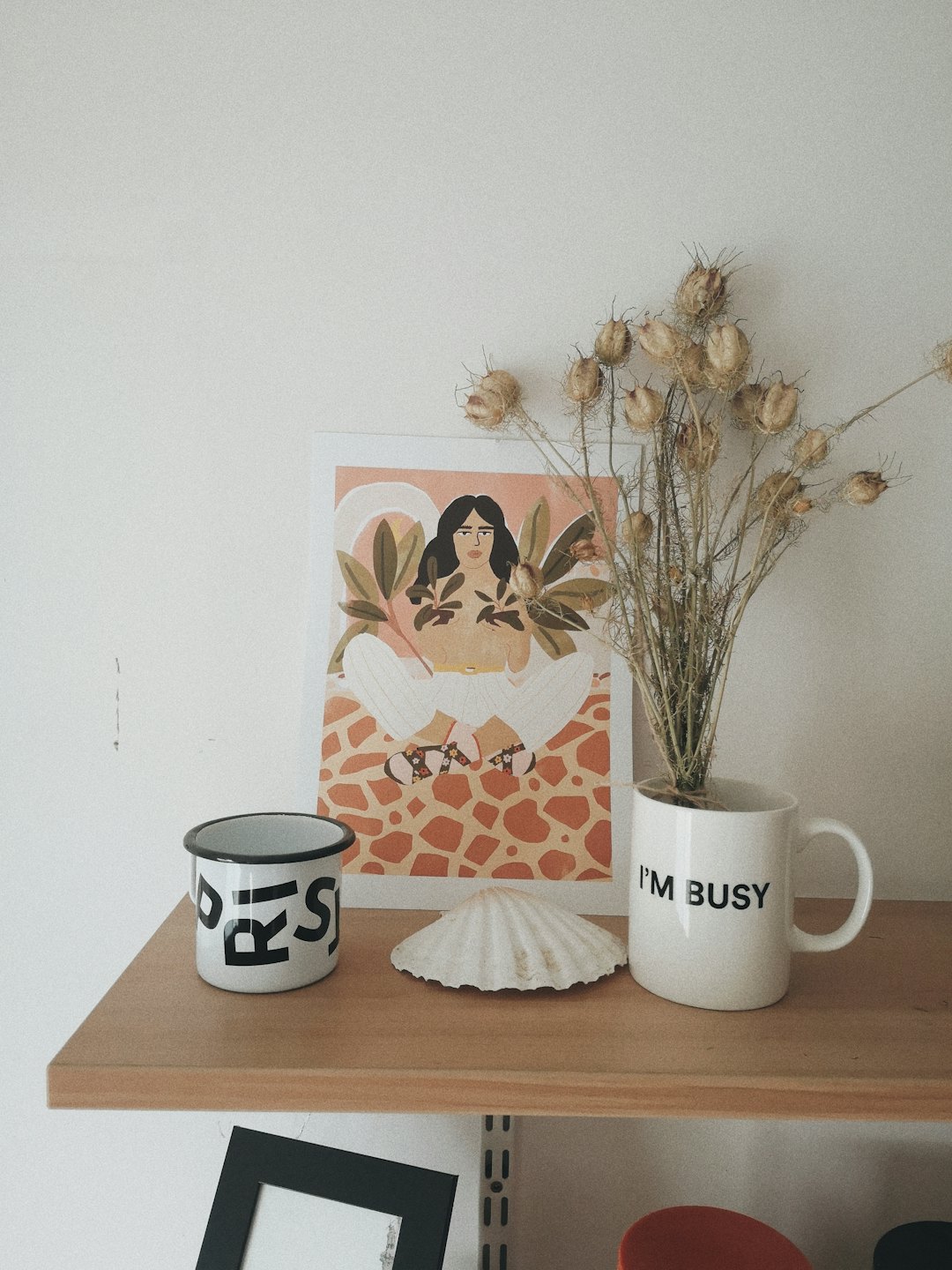 White shelf with decorative mugs, shell, and framed art.